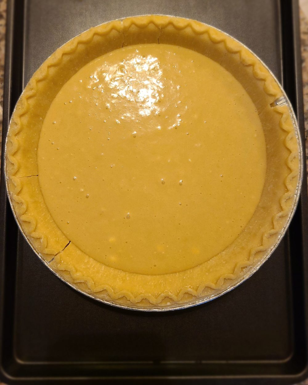 vanilla batter in a pie shell on a dark baking sheet