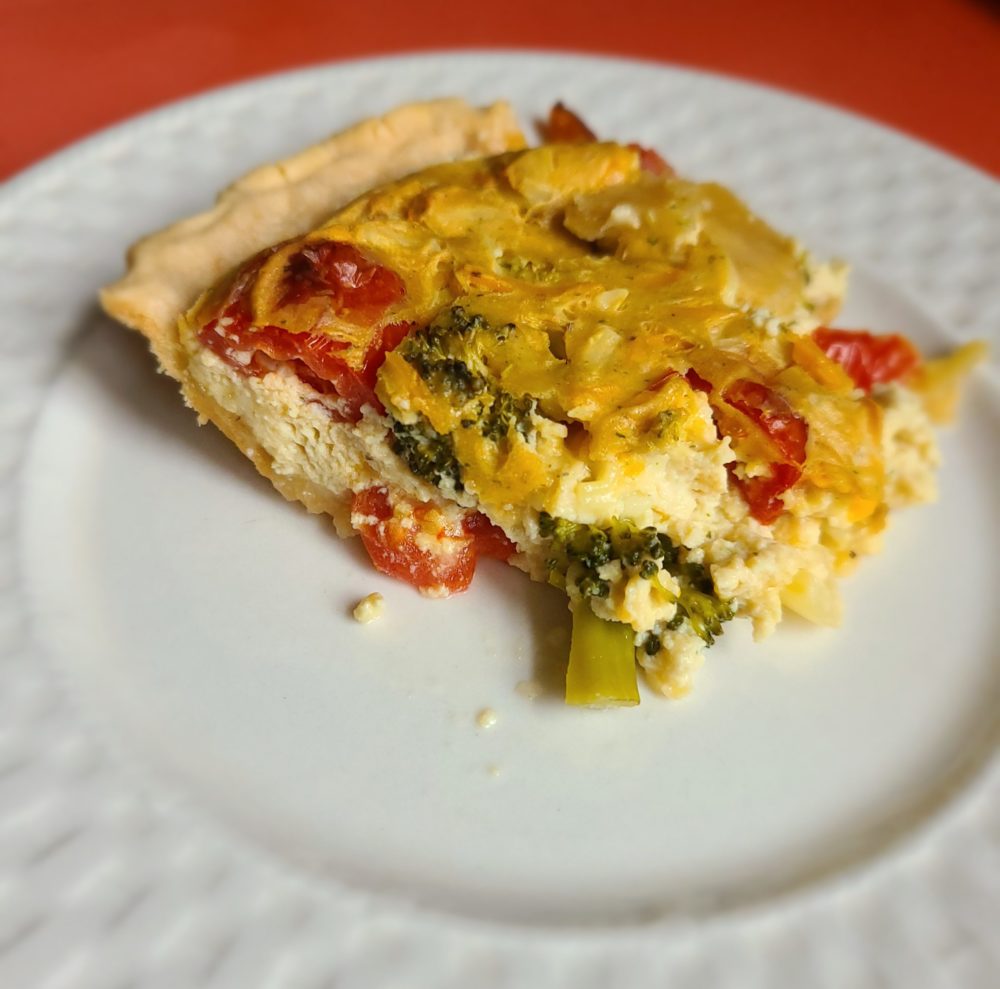 a slice of vegetable quiche on a white plate with an orange background