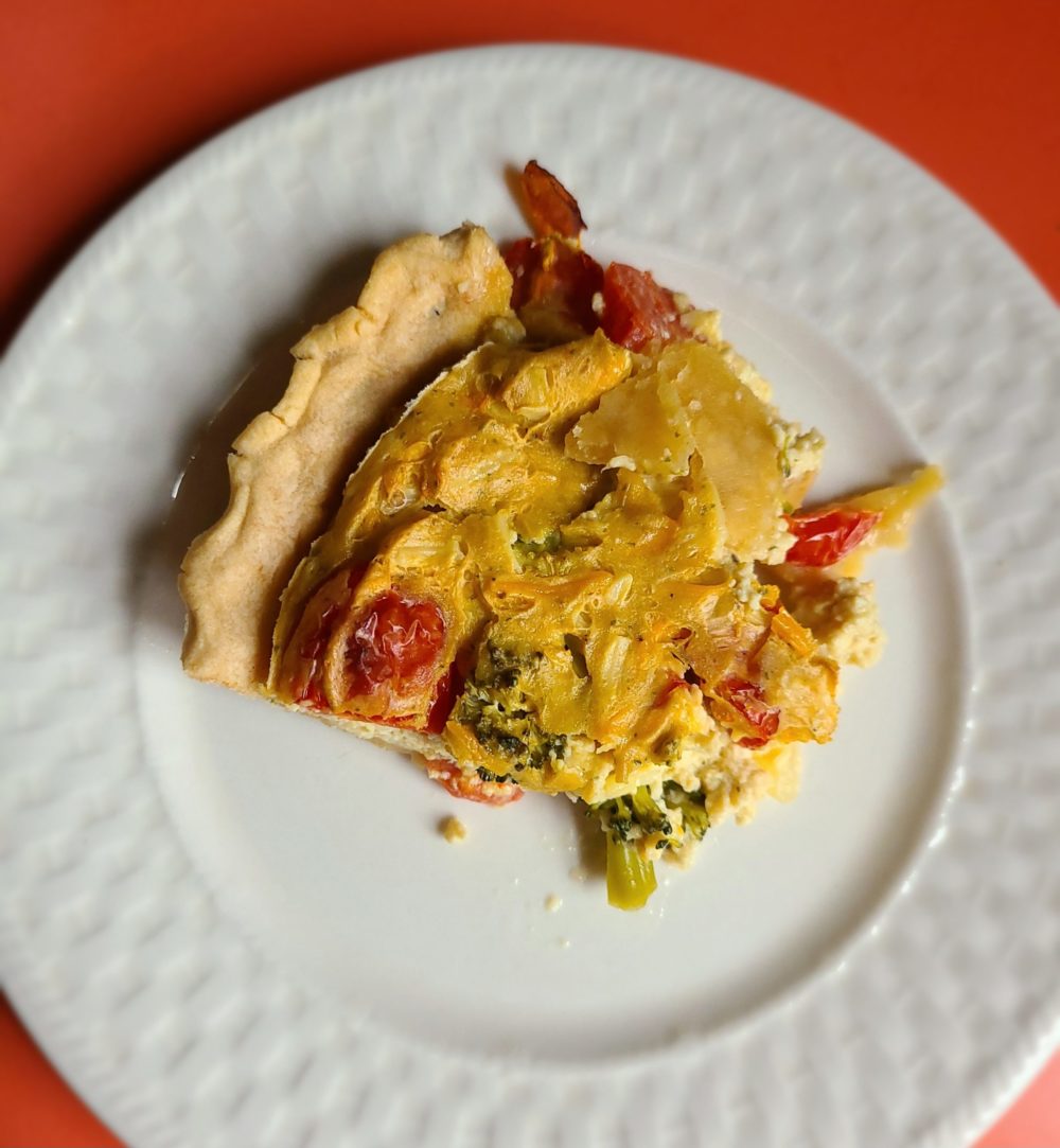 a slice of vegetable quiche on a white plate with an orange background