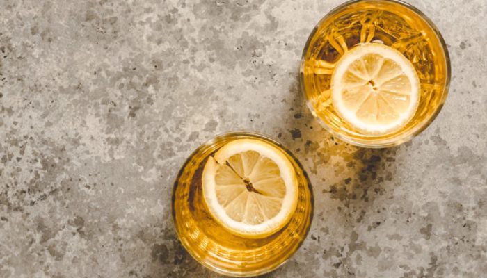two glasses of yellow immune boosting tonic with lemon against a marbled background