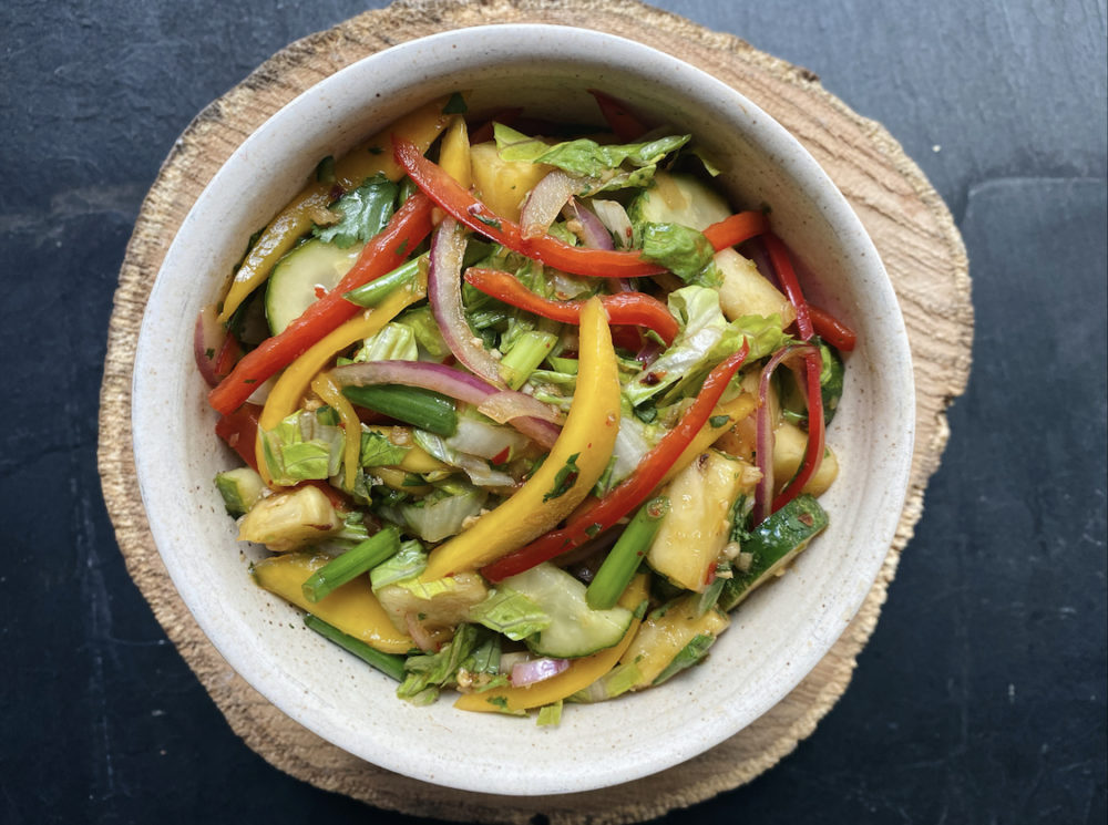 Colorful Asian mango salad in a white bowl on a black countertop.