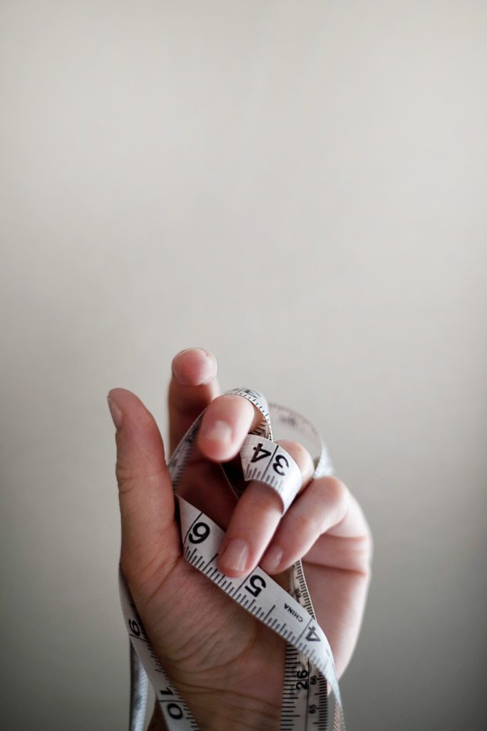 a hand holding a measuring tape against a gray background.