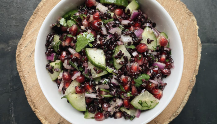 pomegranate black rice cucumber salad in a white bowl against a black countertop.