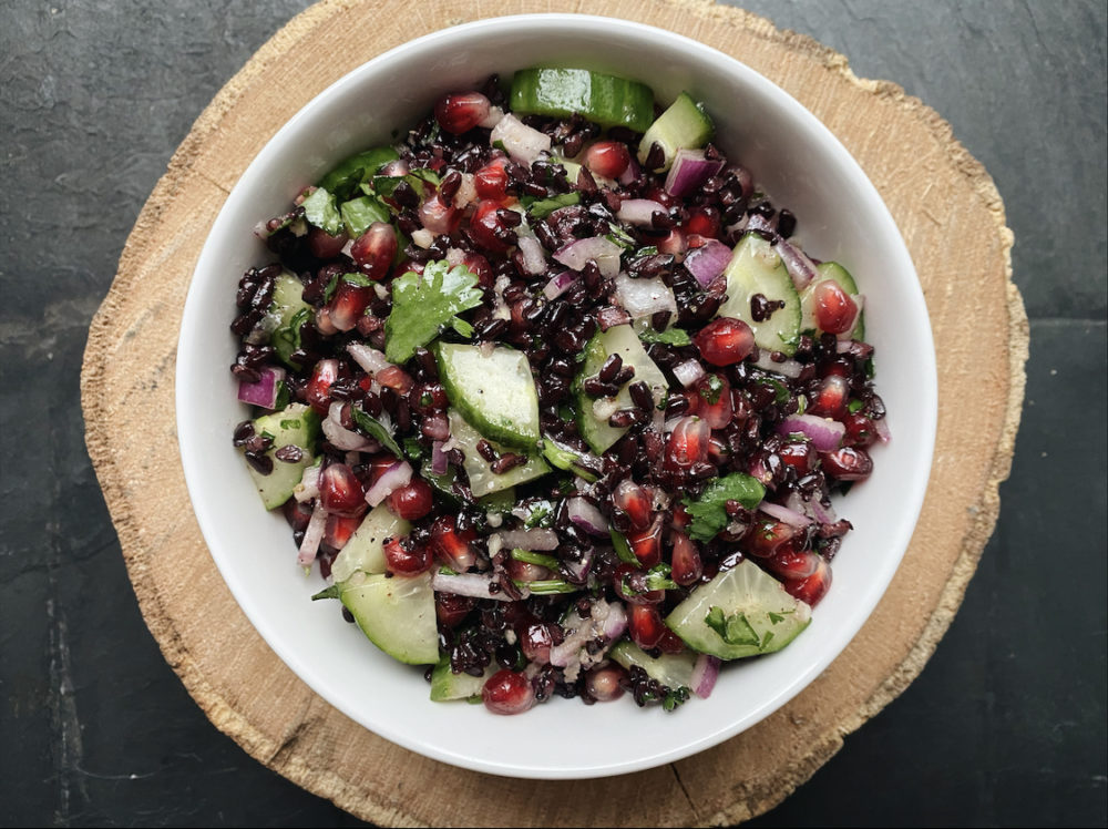 pomegranate black rice cucumber salad in a white bowl against a black countertop.
