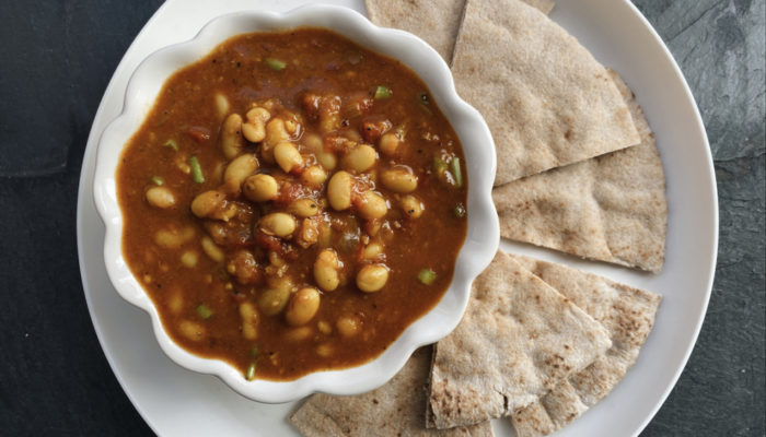 vegan stewed white beans in a bowl, served with pita wedges on a white plate against a black background