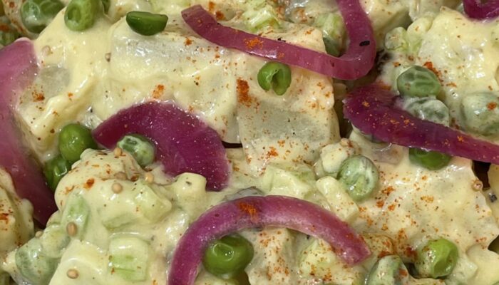 creamy yellow potato salad with peas close-up.