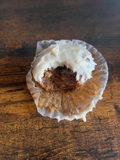 vegan carrot cupcake with a bite taken out of it on a wooden table