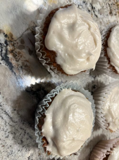 close up of vegan carrot cupcakes with frosting resting on a countertop.