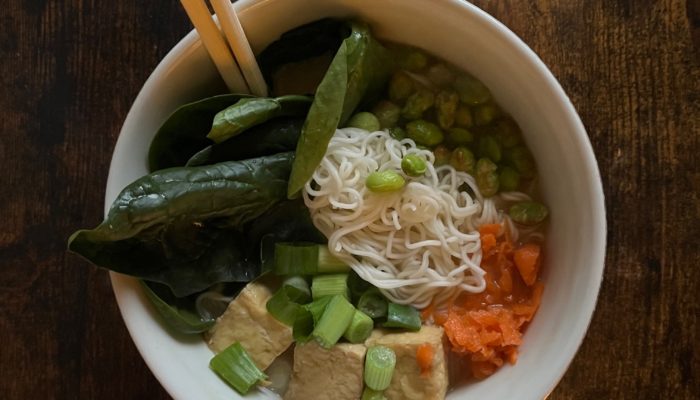 vegan ramen garnished with tofu and vegetables in a white bowl, with wooden chopsticks sticking out of the bowl. It's on a dark brown countertop.
