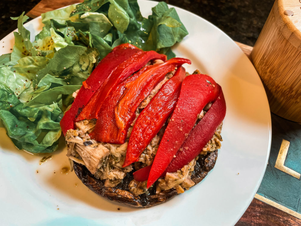 bird's eye view of a stuffed portobello mushroom on a round white plate garnished with a simple baby lettuce salad.