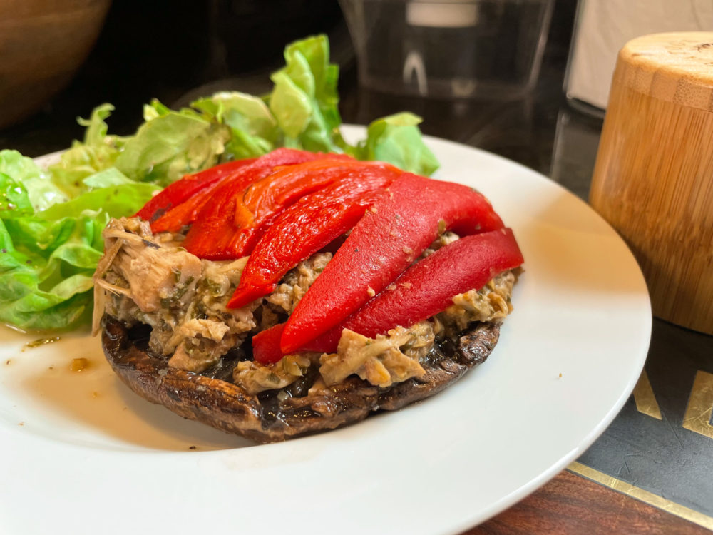stuffed portobello mushroom on a white plate and garnished with lettuce on a table.