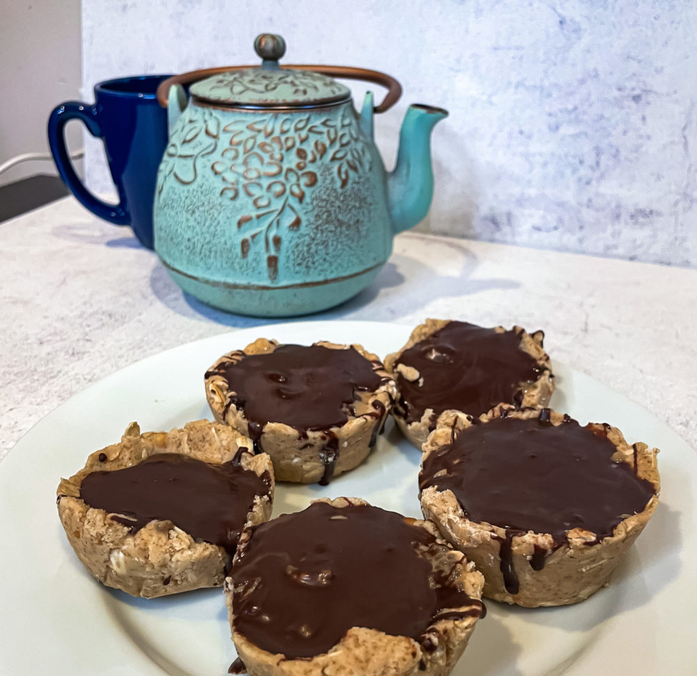 Five chocolate shell chia cups on a round white plate on a white countertop, with a blue teapot in the background.