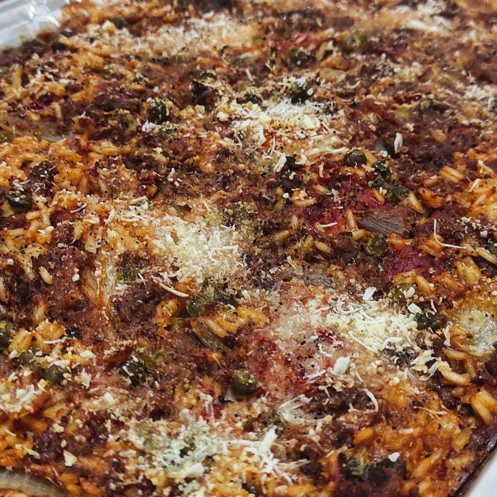 Close-up of Maltese baked rice casserole with vegan cheese sprinkles in a Pyrex dish.