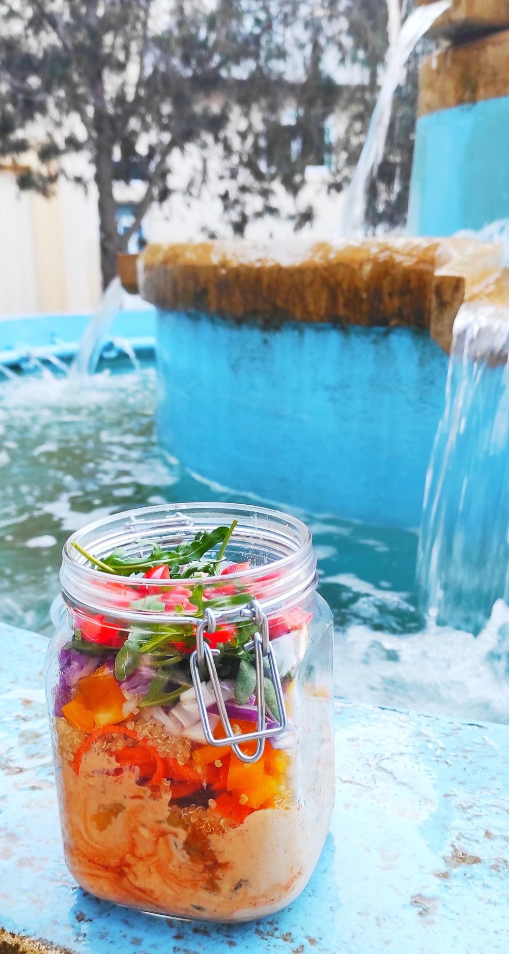 rainbow salad in a mason jar next to a blue-painted fountain in Malta