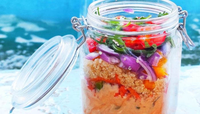 Colorful rainbow salad in a mason jar with the lid open on a light blue table against a medium blue background.