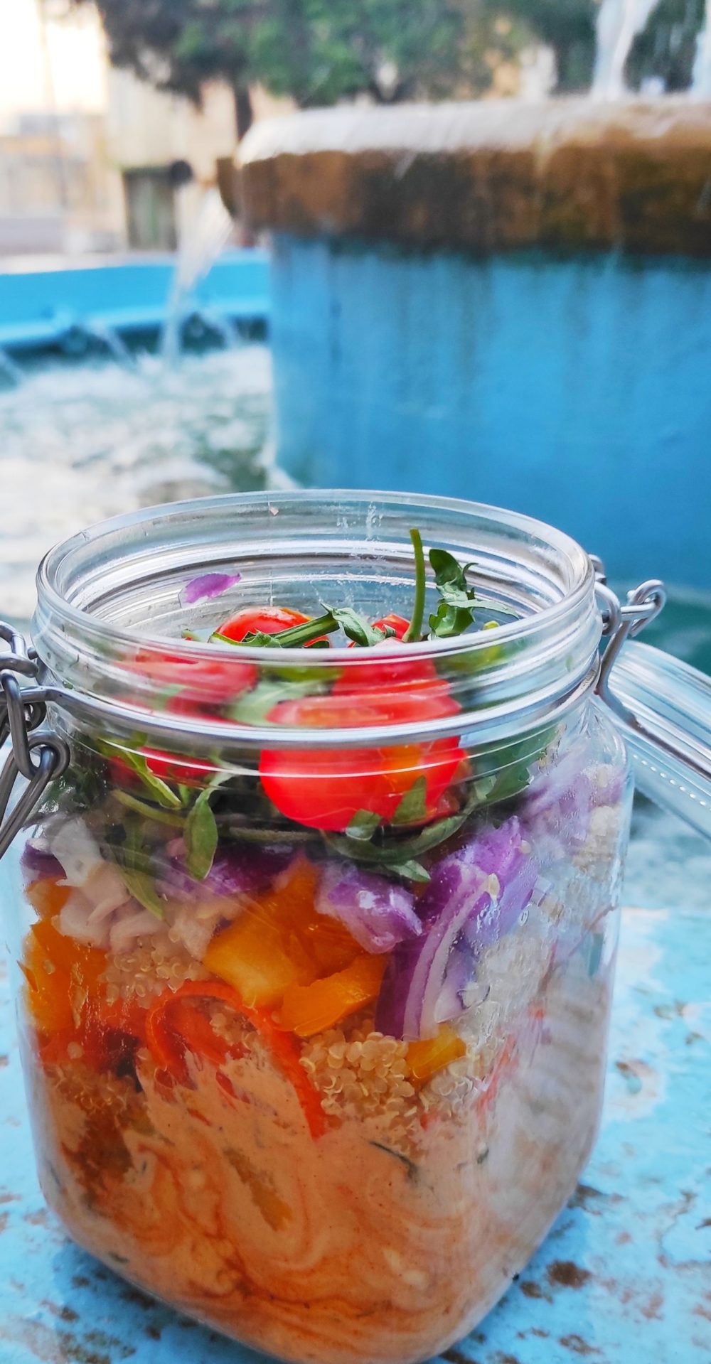 rainbow salad in a mason jar with its lid open. The background shows a blue-painted wall in Malta.