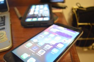 Two iPhones on a wooden desk beside a laptop.