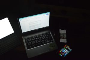 Four glowing devices in a dark room: two laptops and two smartphones.