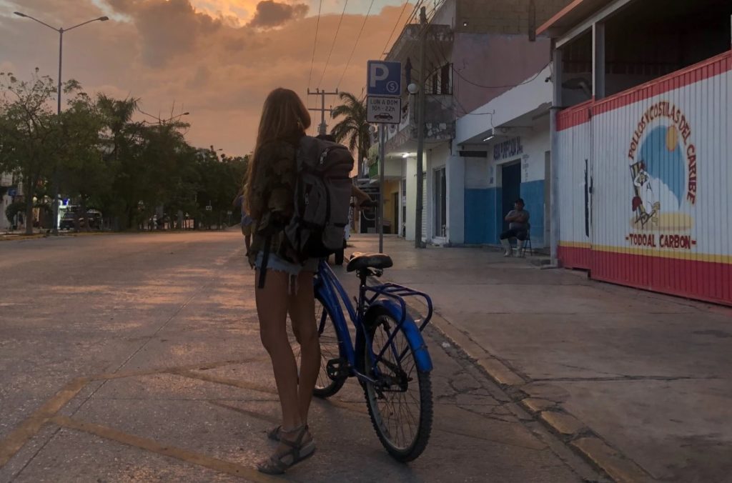 A woman with a backpack and a blue bicycle staring into the twilit sky. 