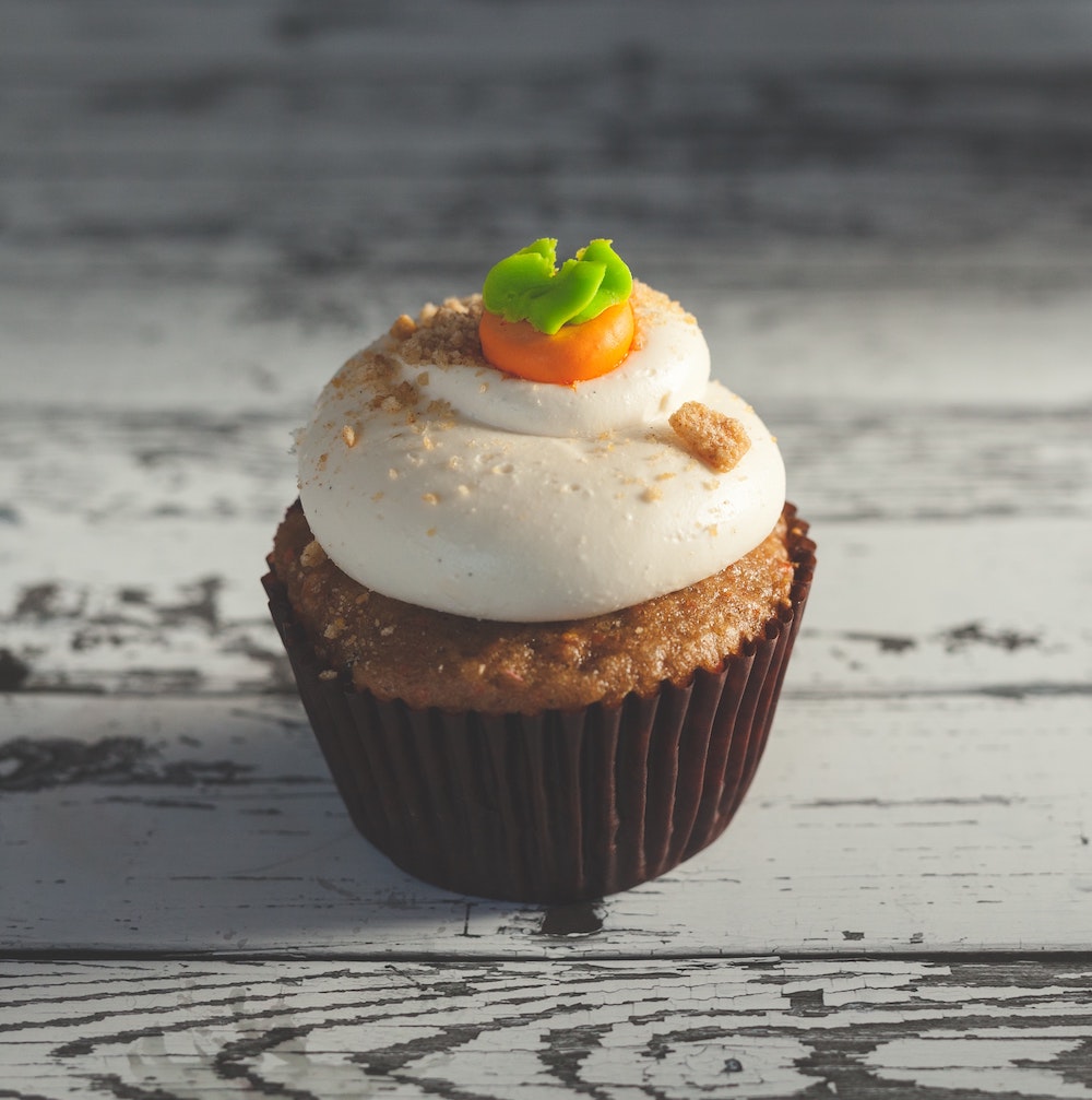 a carrot cupcake with icing on a light wooden background.