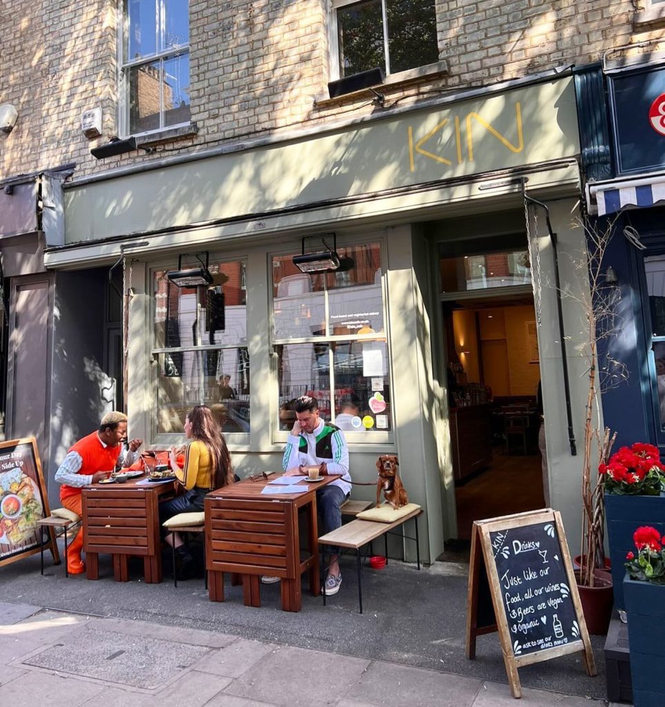 exterior of Kin cafe in London. There are two small tables on the sidewalk and patrons are eating brunch.