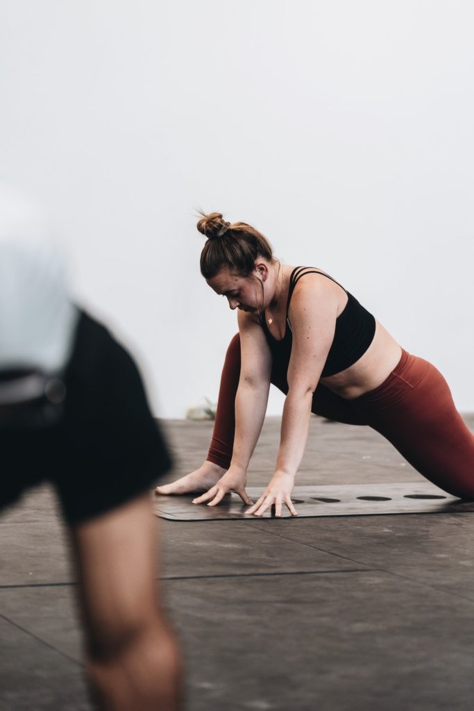 a white woman in a black sports bra and rust red leggings doing a low lunge stretch. 