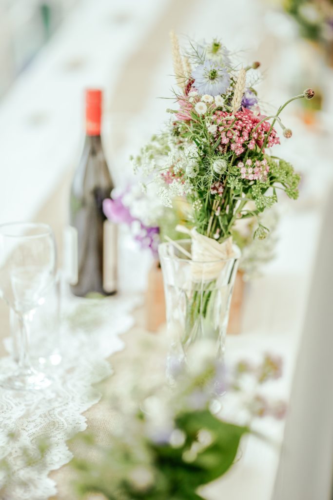 flowers in champagne glass on a long white table set for a wedding. 