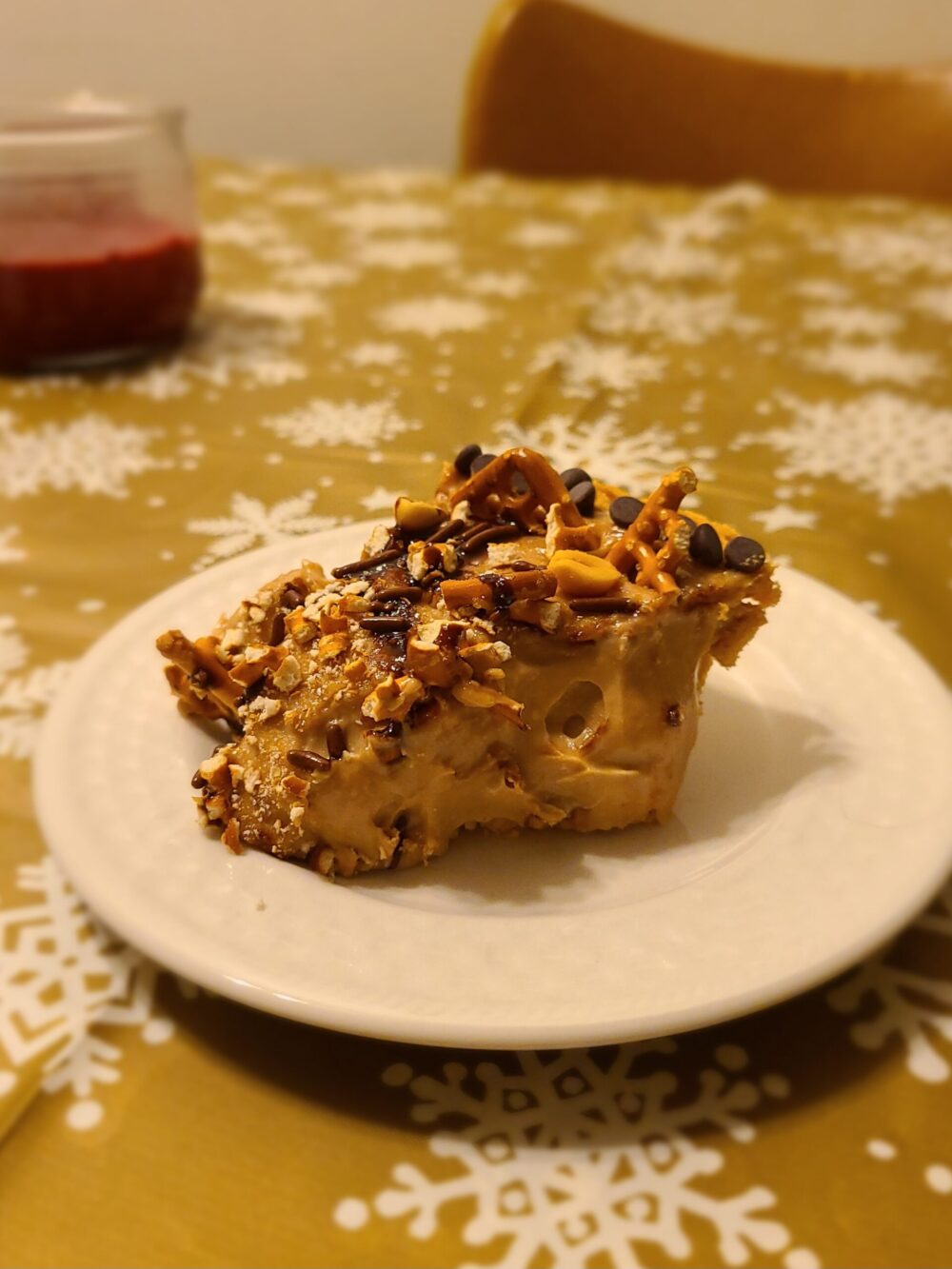 a slice of vegan chocolate peanut butter pretzel pie on a white plate against a tablecloth with snowflakes