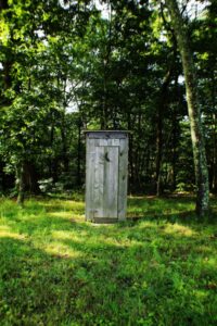 a wooden outhouse in the middle of a forest.