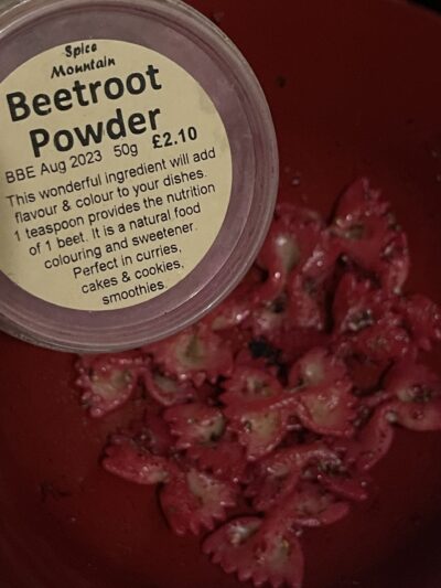 beetroot powder in a tub next to red-stained bow-shaped pasta.