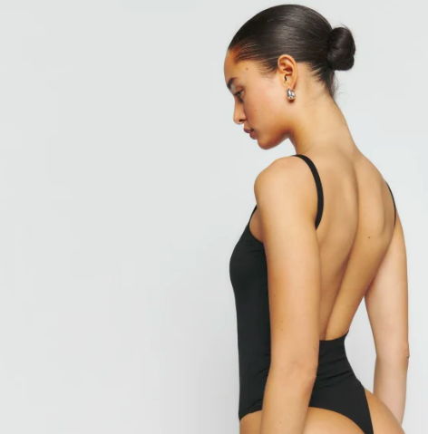 a model wearing a skinny strap black body suit, shown from the back.