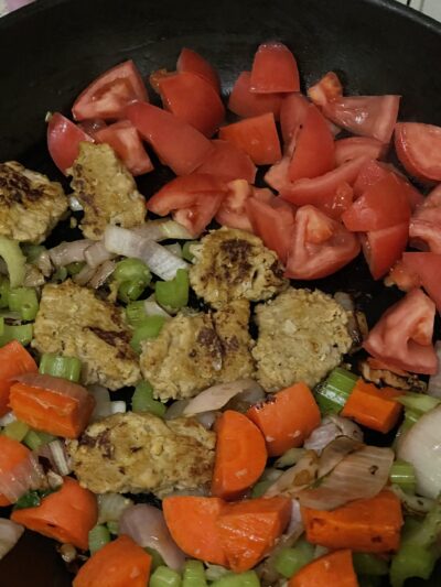 seitan, onion, carrot, celery, and tomato mixture in a pot.