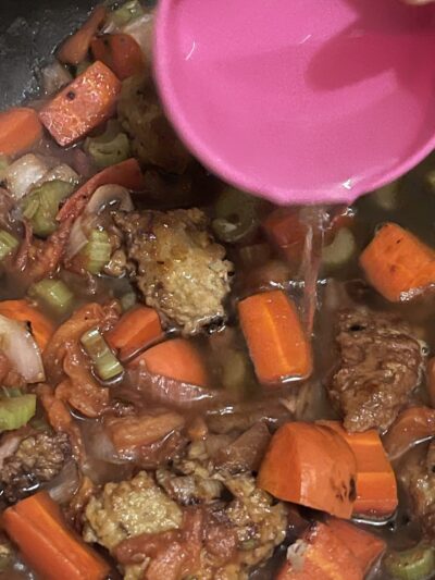 adding water using a small bowl to the vegan beef stew in a pot.