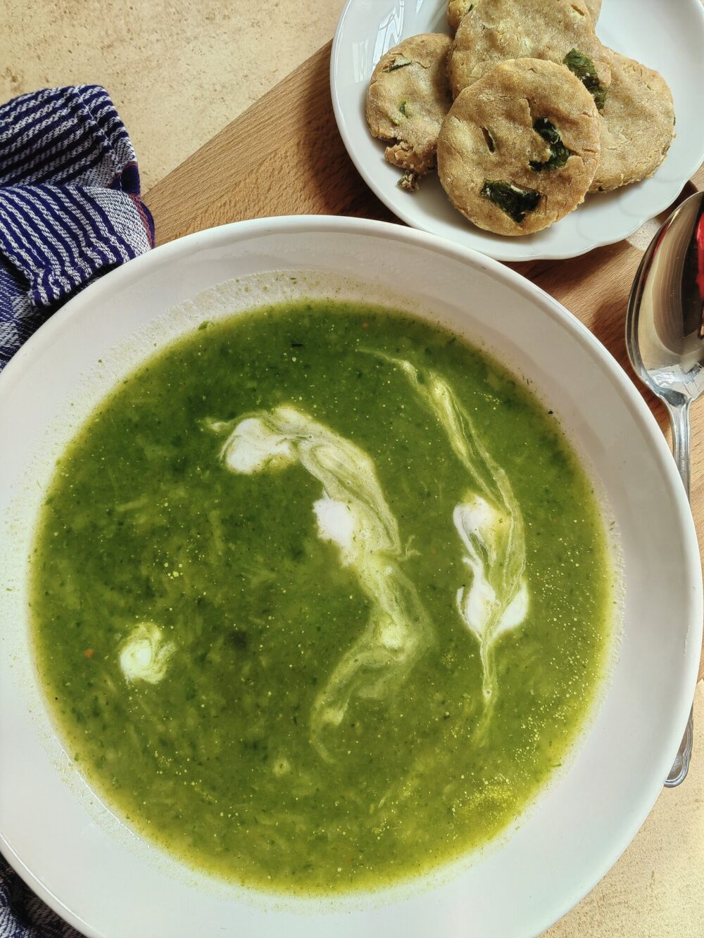 creamy green wild garlic soup in a white bowl on a wooden table with some crackers on the side.