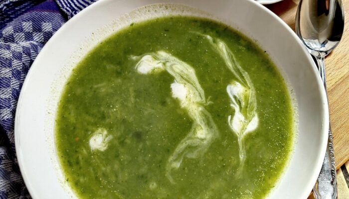 creamy green wild garlic soup in a white bowl on a wooden table with some crackers on the side.