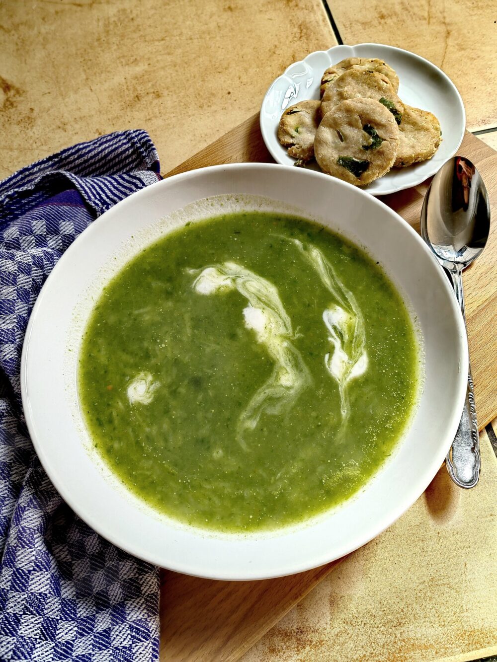 creamy green wild garlic soup in a white bowl on a wooden table with some crackers on the side.