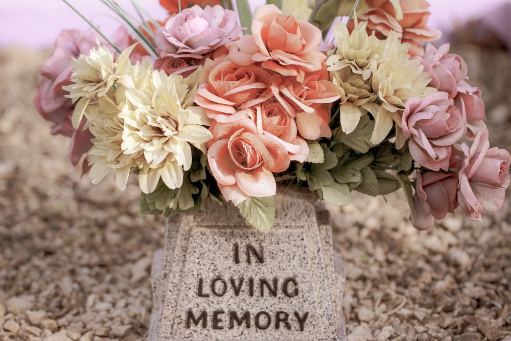 A stone vase inscribed with "in loving memory" and containing pink and ivory flowers.