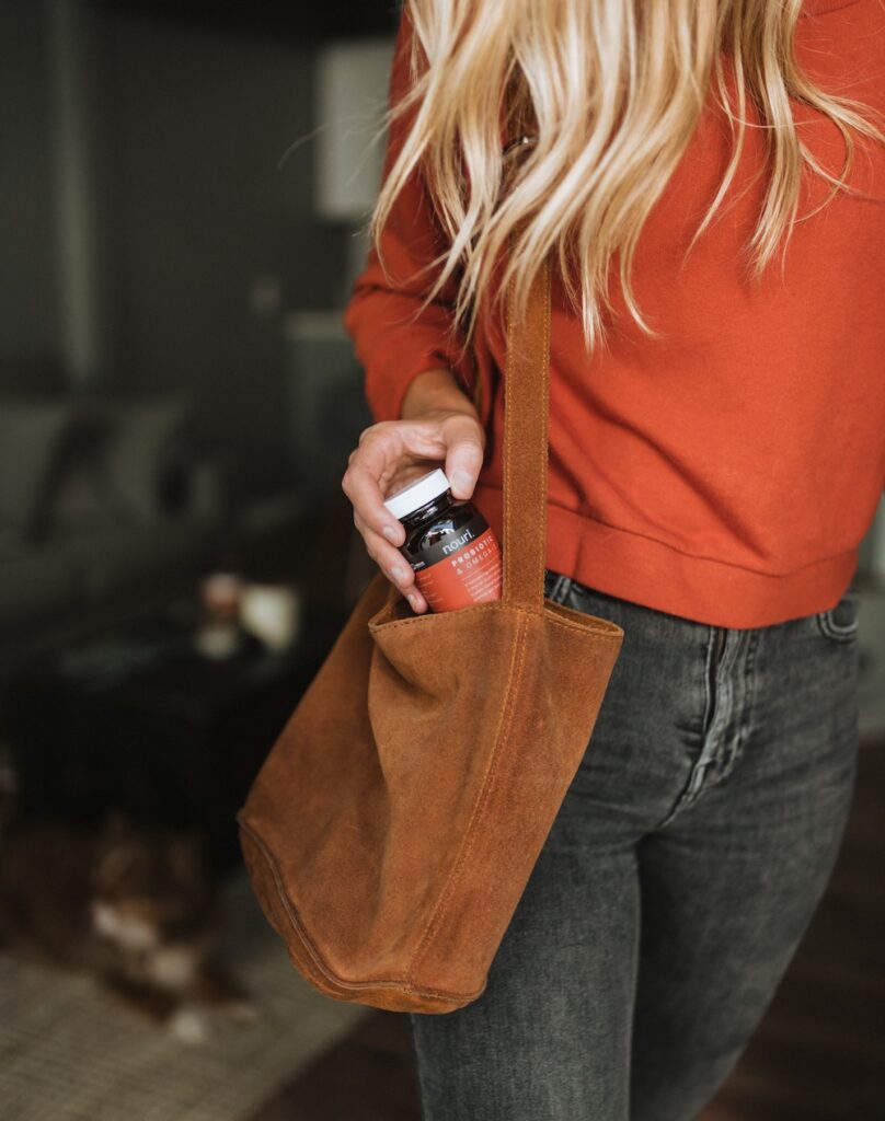 a blonde woman is taking out a bottle of supplements from her brown bag. 