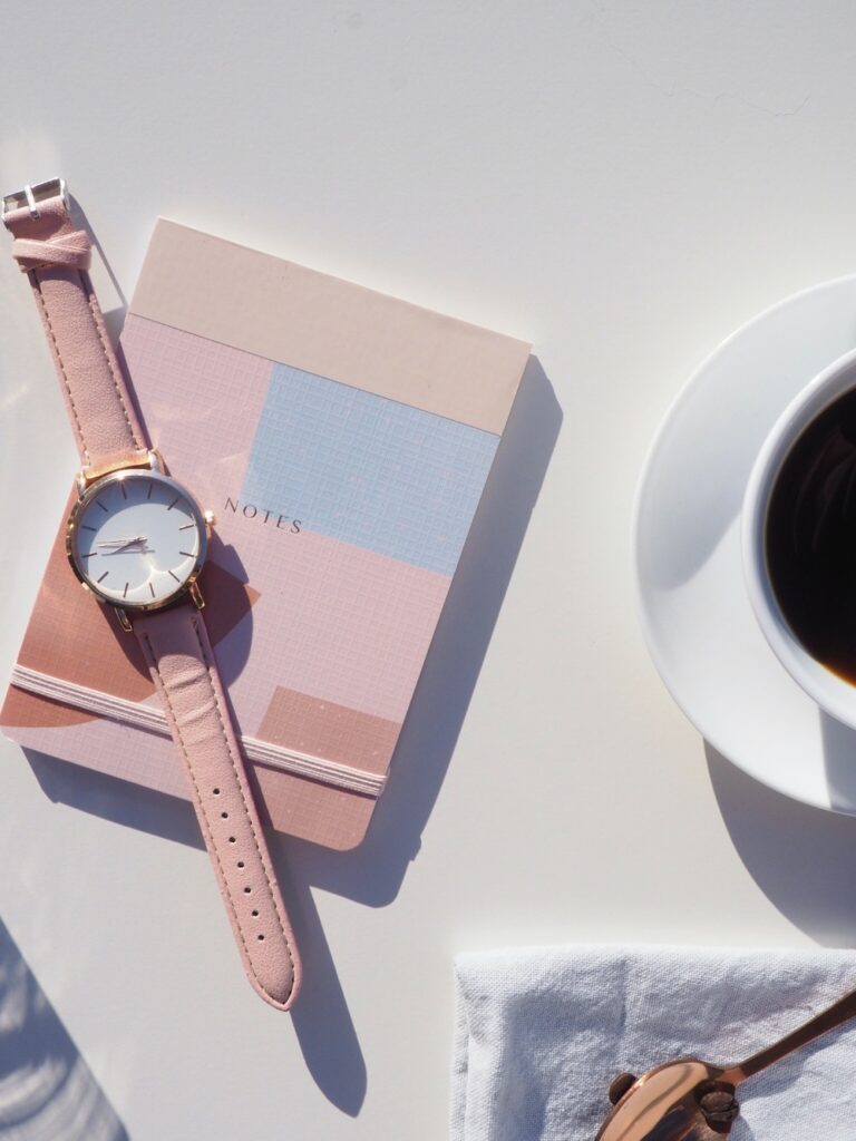 a pink watch on a pink journal on a white table.
