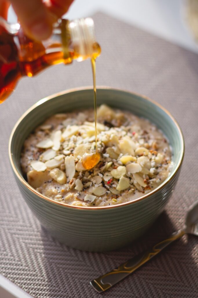 pouring maple syrup into a bowl of oatmeal in a light blue bowl on a wooden table. 