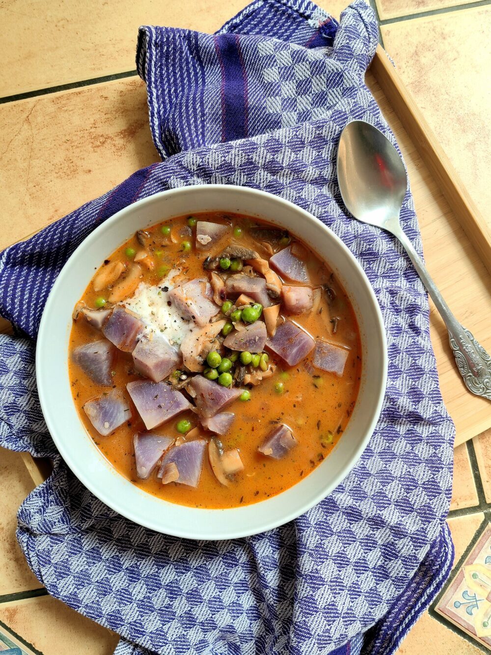 bird's eye view of an orange-colored Peruvian vegan soup in a white bowl, over a blue tea towel and next to a spoon.