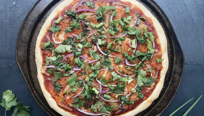 vegan kimchi pizza on a black pan on a black stone countertop with cilantro springs next to it