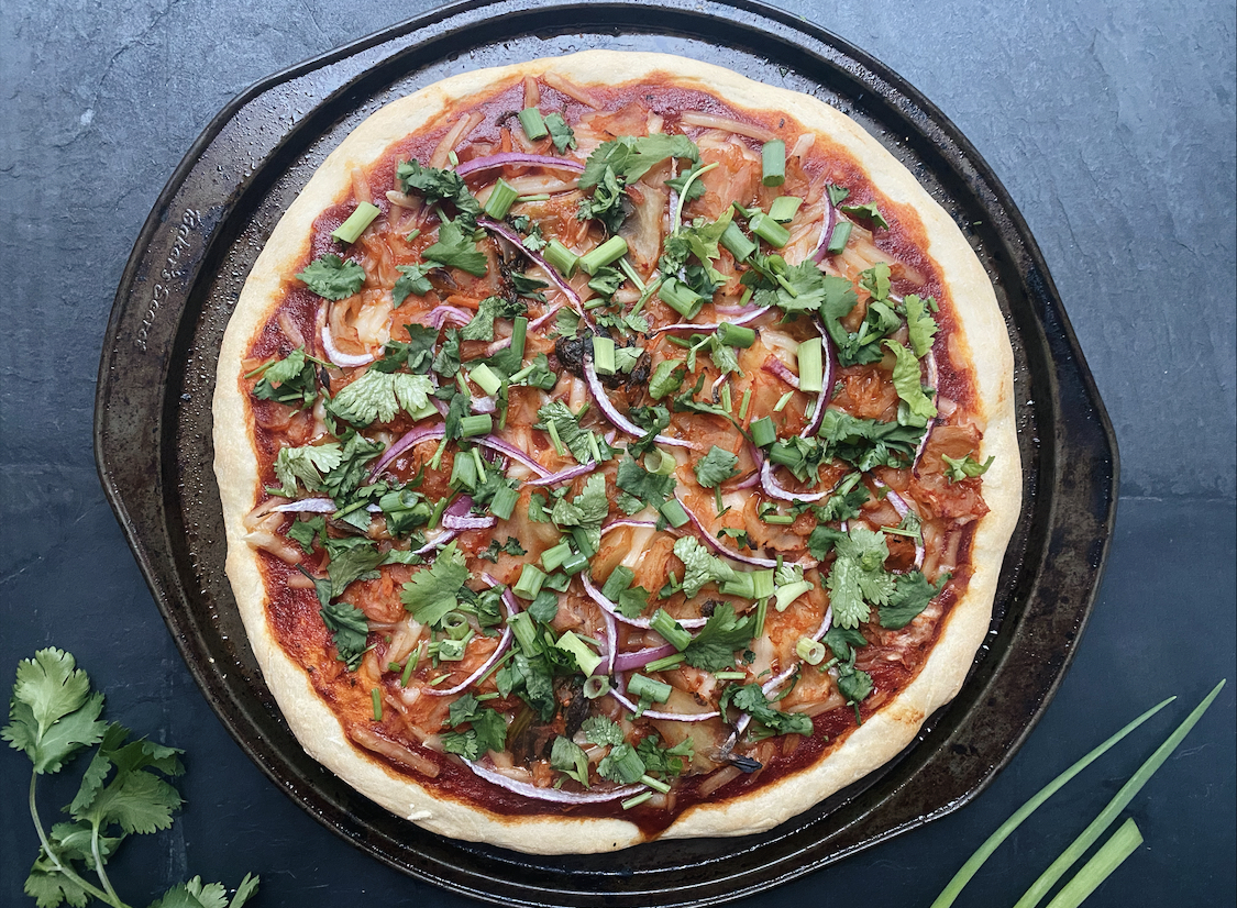 vegan kimchi pizza on a black pan on a black stone countertop with cilantro springs next to it