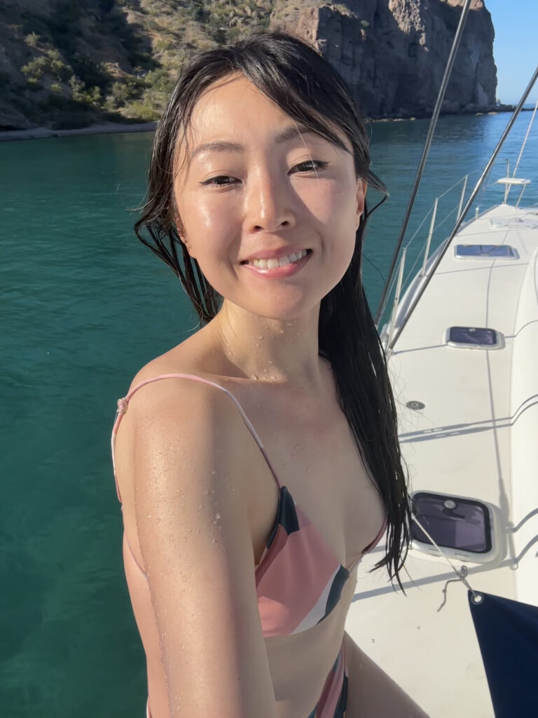 a selfie of an Asian woman wearing a bikini and sitting on a white boat against the background of the sea.
