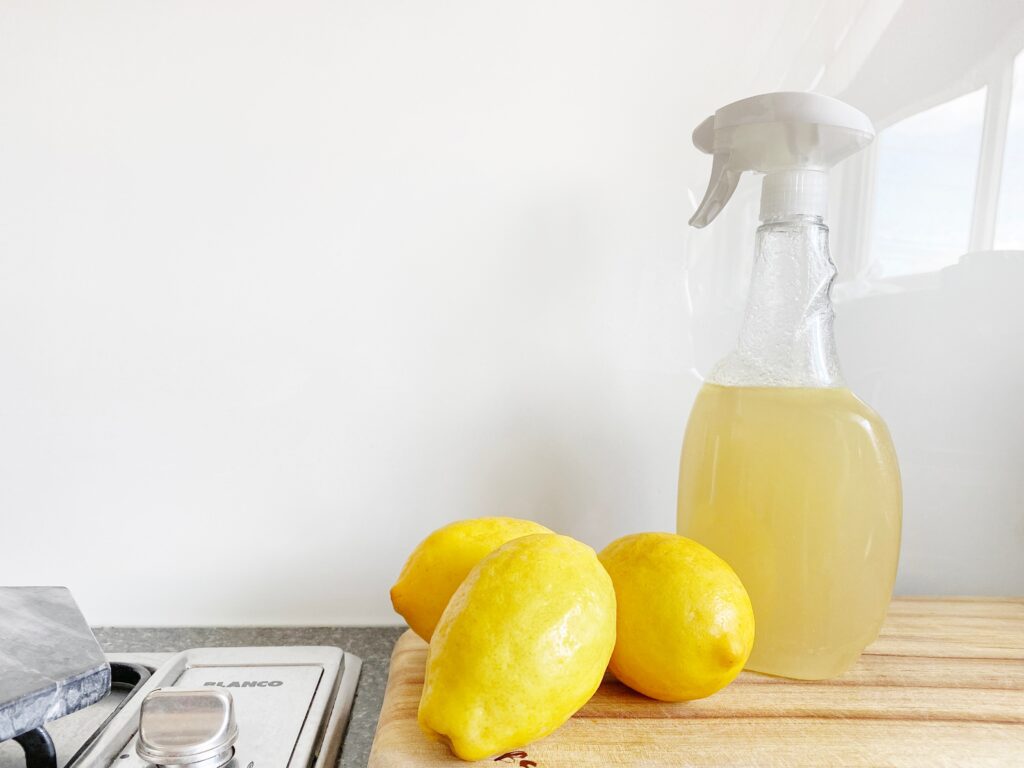 A bottle of Vinegar cleaning solution and some lemons sit on a desk. 