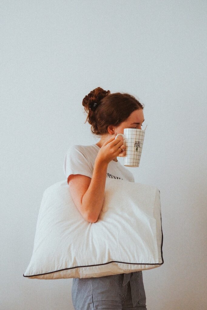 a woman looking tired and holding a pillow and a mug.