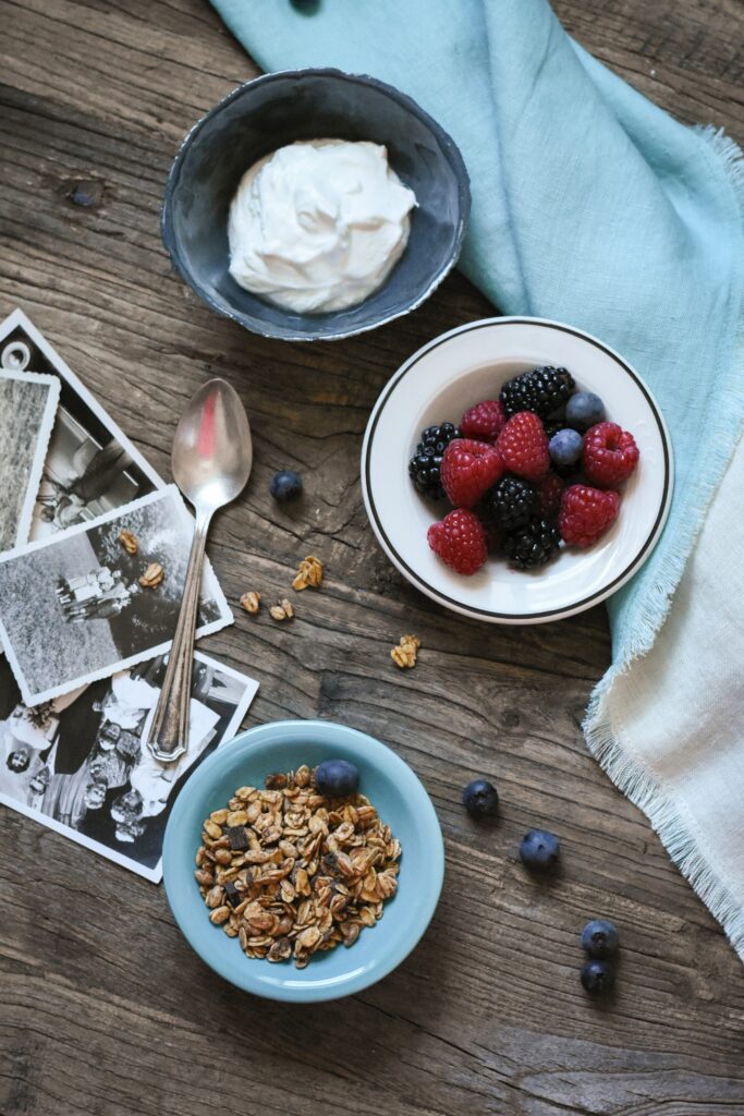 bowl of yogurt, bowl of berries, and bowl of granola on a wood table with photos