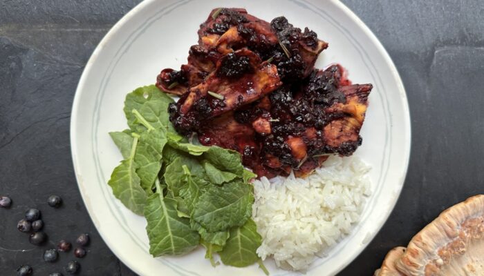 chicken of the woods dish glazed with blueberry balsamic sauce, garnished with herbs and white rice on a white plate on a black countertop.