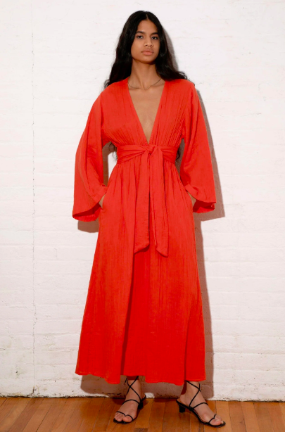 a model wearing a warm red coverup dress with a deep v neckline and tie at the waist.