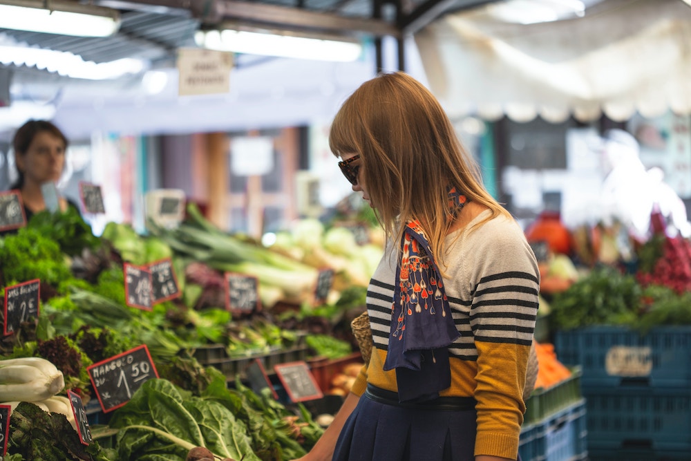 a woman wearing a scarf and a striped sweater is shopping for vegetables in a market.